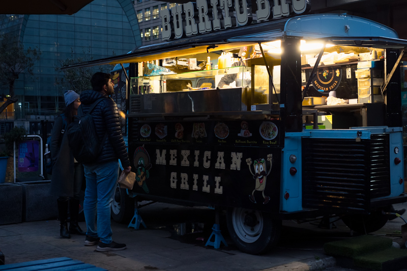 A couple choosing burritos at a vintage food truck van in London Canary Wharf at night